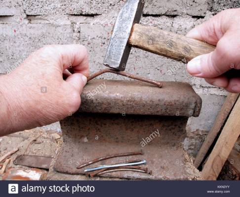 hands-straightening-curved-nails-with-hammer-on-old-rusty-rail-piece-KKN3YY.jpg